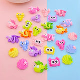 Lot de figurines Poisson Multicolore disposées sur un fond rose et bleu, présentant différents modèles colorés (poissons, crabes, coquillages).
