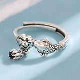 Bague Poisson Couleur Argent Ajustable sur fond bleu, mettant l’accent sur le design de la queue et la tête de poisson