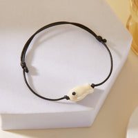 Gros plan sur le Bracelet Poisson Blanc Nacré Ajustable, posé sur un support, soulignant la finition irisée du poisson.