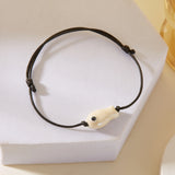 Gros plan sur le Bracelet Poisson Blanc Nacré Ajustable, posé sur un support, soulignant la finition irisée du poisson.