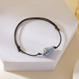 Bracelet Poisson Gris Ajustable, posé sur un support, mettant en évidence le pendentif poisson en céramique.