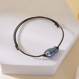 Bracelet Poisson Noir Ajustable, présentant un pendentif en forme de poisson monté sur un cordon noué.