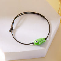 Gros plan sur le Bracelet Poisson Vert Ajustable posé sur un support, affichant le design minimaliste du pendentif