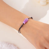 Bracelet Poisson Violet Ajustable, porté au poignet, présentant un pendentif en céramique sur cordon noir.