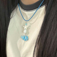 Collier Poisson Bleu Pastel avec Étoile de Mer, porté autour du cou, mettant en valeur un pendentif combinant poisson translucide, perles et étoile de mer.