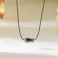 Gros plan sur le Collier Poisson Noir sur Cordon Ajustable, présentant un pendentif en forme de poisson minimaliste.