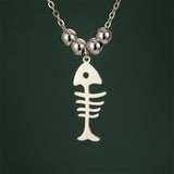 Détails du pendentif du Collier Poisson Squelette Argenté à Billes, mettant en évidence la silhouette ajourée de l’arête de poisson.

