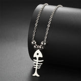 Gros plan sur le Collier Poisson Squelette Argenté à Billes, posé sur un support noir, avec ses perles métalliques et son pendentif minimaliste.