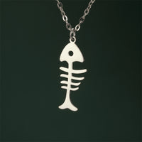 Gros plan sur le Collier Poisson Squelette Argenté, présenté sur fond vert, mettant en évidence la silhouette ajourée du pendentif.