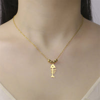 Collier Poisson Squelette Doré à Billes porté autour du cou, mettant en avant les perles dorées et le pendentif ajouré.