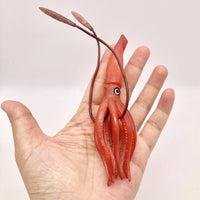 Figurine Calamar Rouge présentée dans une main, permettant d’apprécier sa taille et sa forme élancée.