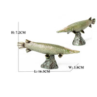 Figurine Poisson Alligator Gar en résine, avec un aspect vert métallique et un long museau, présentée sur un socle rocheux.
