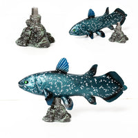 Figurine poisson coelacanthe bleue posée sur un socle rocheux, vue latérale
