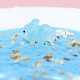 Figurine Poisson Exotique Bleu en résine, posée sur du sable coloré, avec une étoile de mer à proximité.
