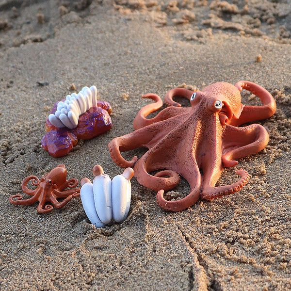 Figurine Poulpe disposée sur le sable avec d’autres éléments marins, illustrant son aspect réaliste et sa couleur orangée