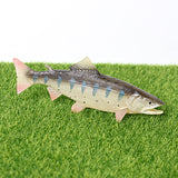 Figurine Saumon Arc-en-Ciel posée sur gazon synthétique, montrant son profil et ses motifs argentés et bleutés.
