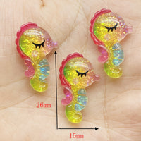 Lot de figurines Hippocampe Arc-en-Ciel en résine pailletée, mesurant environ 26 mm x 15 mm, présentées dans la main pour illustrer leur taille.
