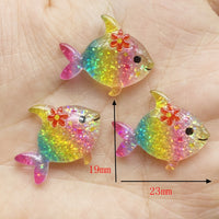 Lot de figurines Poisson Arc-en-Ciel en résine transparente et pailletée, décorées d'une fleur, mesurant environ 23 mm x 19 mm, présentées dans la main pour illustrer leur taille.