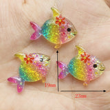 Lot de figurines Poisson Arc-en-Ciel en résine transparente et pailletée, décorées d'une fleur, mesurant environ 23 mm x 19 mm, présentées dans la main pour illustrer leur taille.